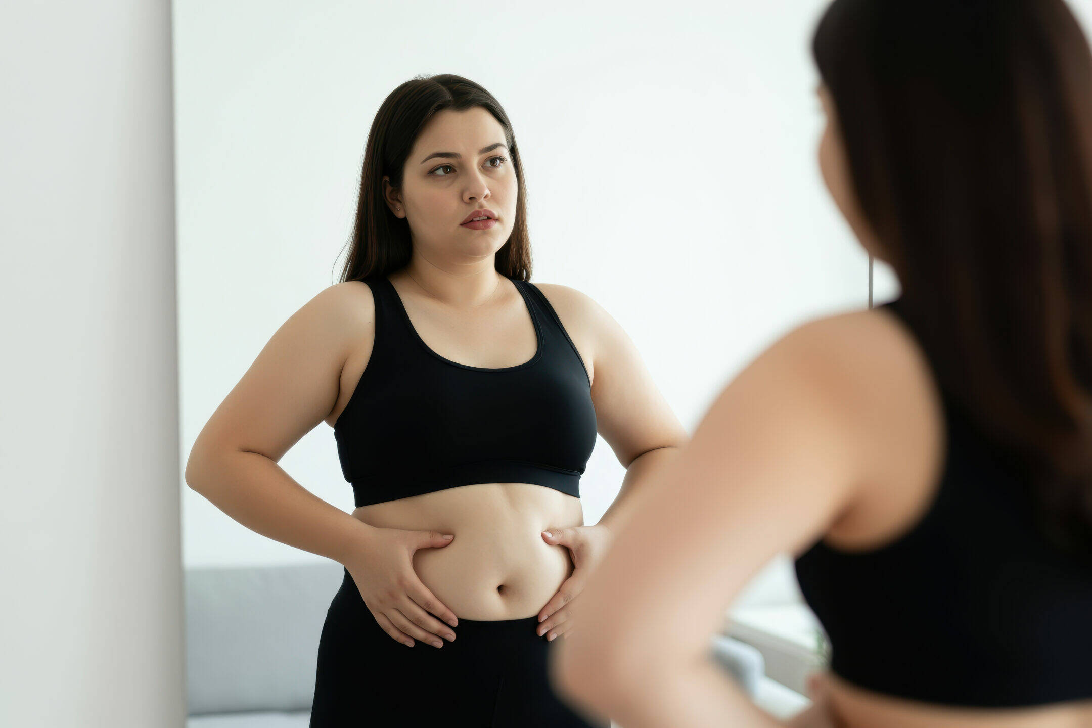Femme observant son ventre dans un miroir, les mains posées sur l’abdomen