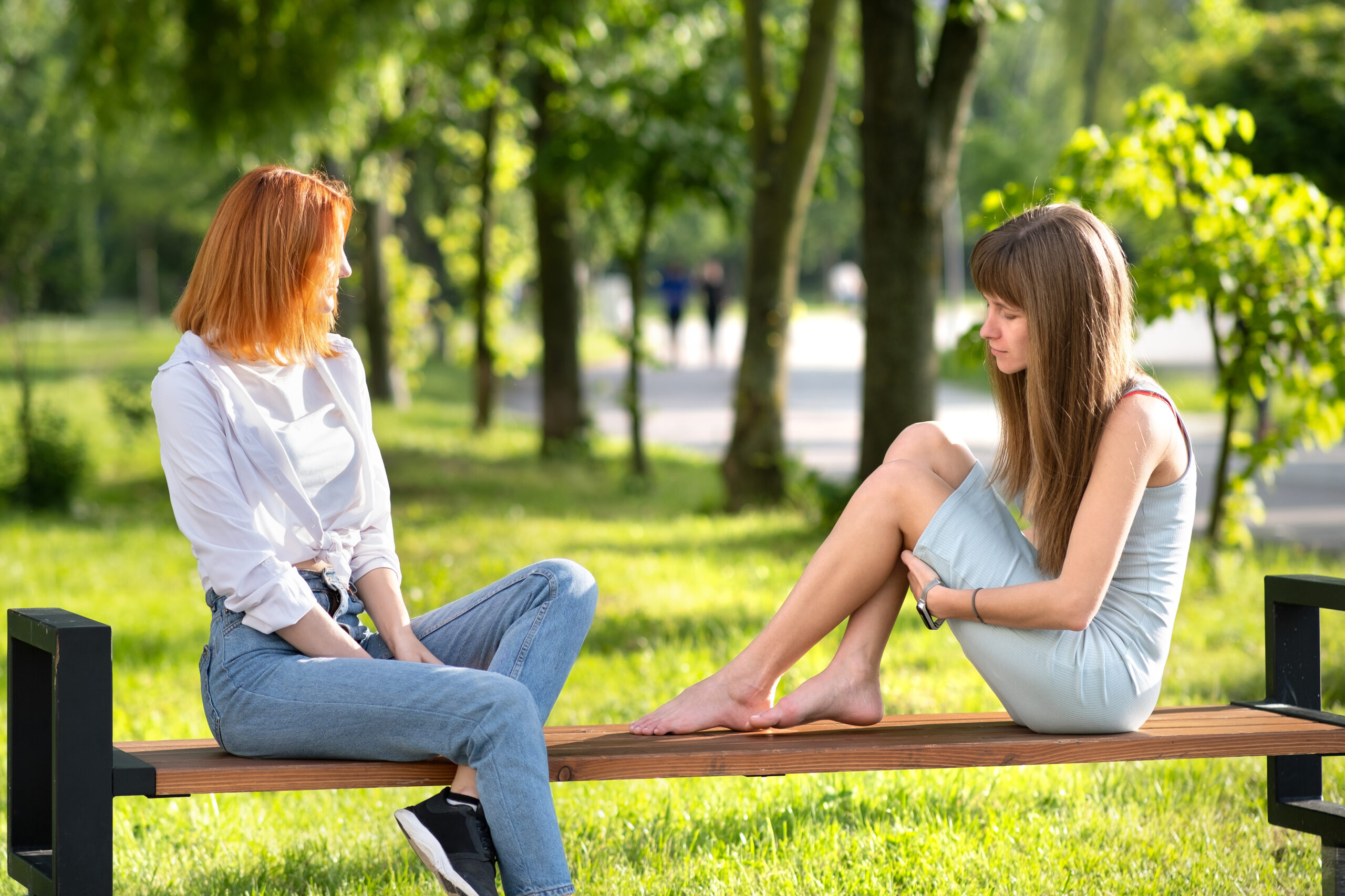 Deux femmes assises sur un banc dans un parc, tournées l’une vers l’autre en position d'échange